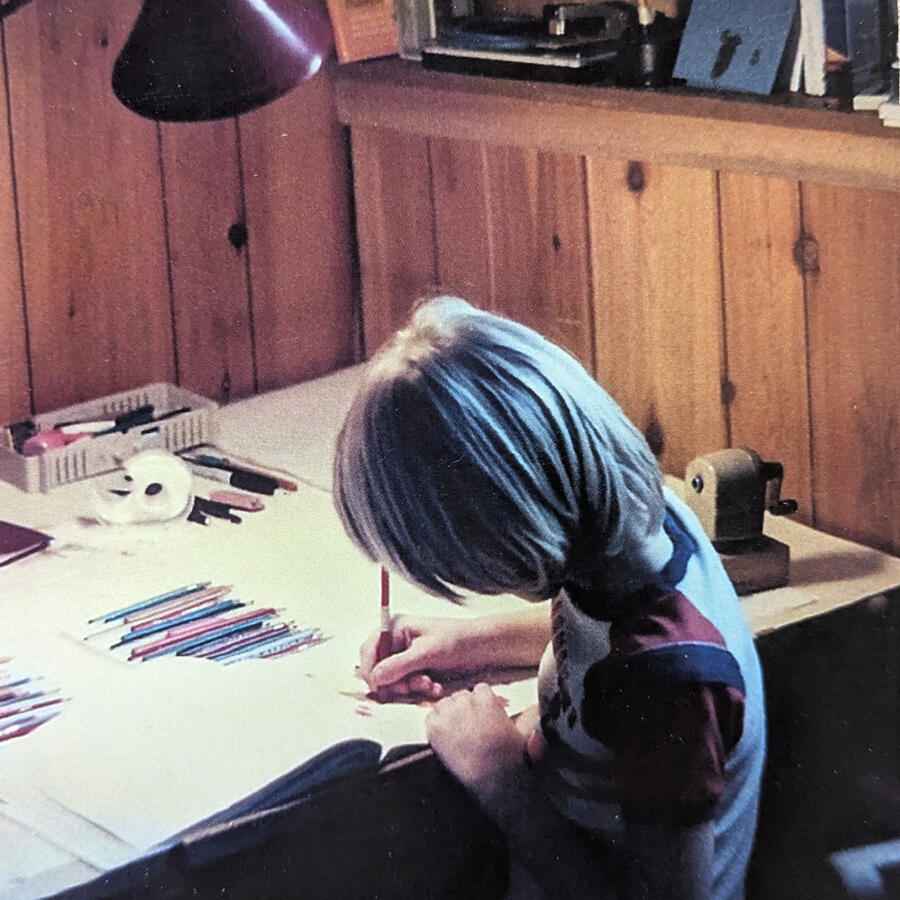 Lil Sarah at work Small blonde child sitting at a table doing art with colored pencils.
